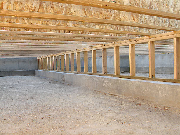 This color photo shows a view of the crawlspace foundation beneath the framing of a new house under construction. Floor joists and a pony wall (short support wall) on a concrete footer are clearly visible. The crawlspace floor is neat and clean. The image is in landscape orientation.