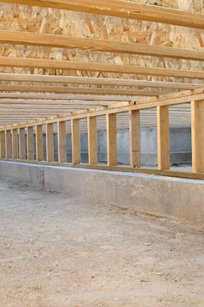 This color photo shows a view of the crawlspace foundation beneath the framing of a new house under construction. Floor joists and a pony wall (short support wall) on a concrete footer are clearly visible. The crawlspace floor is neat and clean. The image is in landscape orientation.